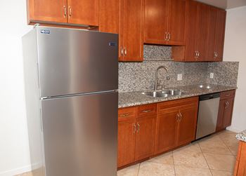 A stainless steel refrigerator stands in a kitchen with wooden cabinets.